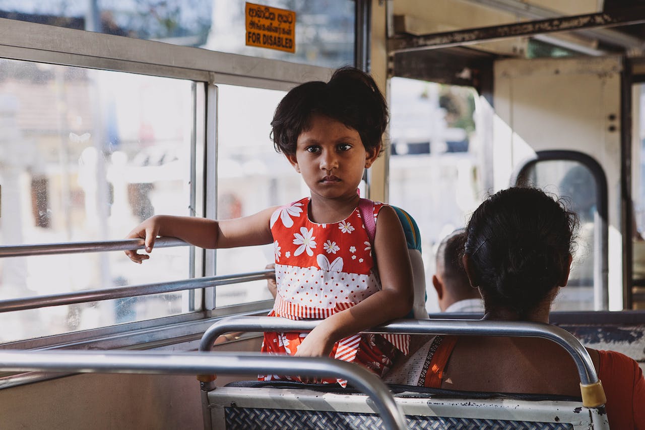 Mastering the First Impression: Your intriguing post title goes here A young girl in a red dress holds onto a rail in a Sri Lankan public bus interior scene.